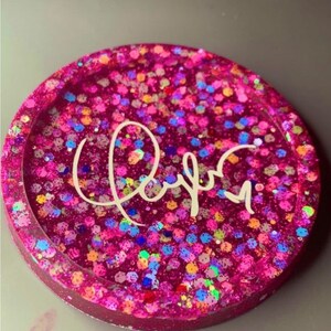 K&ouml;nnte beinhalten: Rosa glitzernder Harz-Untersetzer mit einer wei&szlig;en Aufschrift "Rayna".