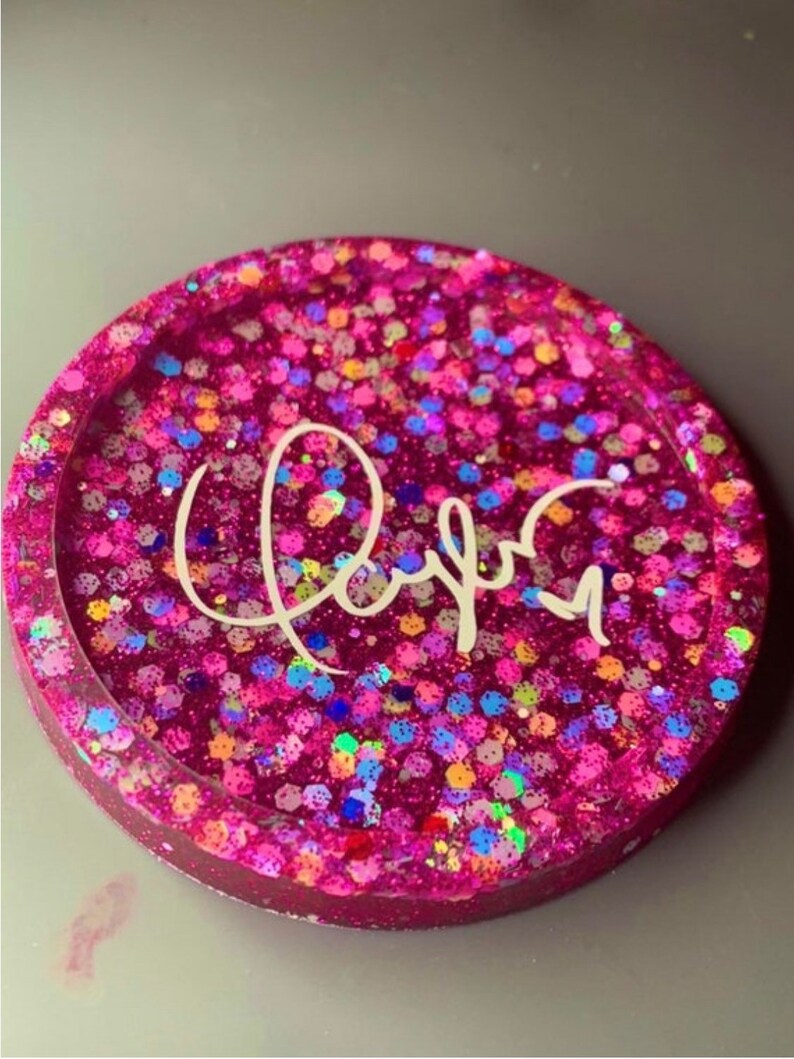K&ouml;nnte beinhalten: Rosa glitzernder Harz-Untersetzer mit einer wei&szlig;en Aufschrift "Rayna".