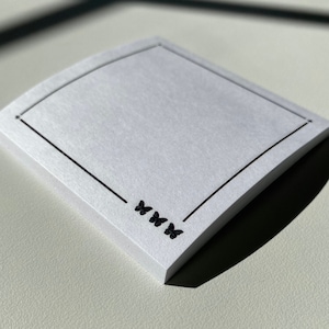 May include: White square sticky note with a black border and four black butterfly silhouettes in the bottom right corner. The note is slightly curved.