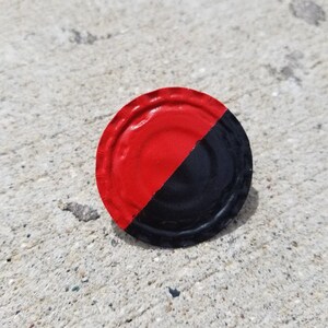 Puede incluir: Un disco metálico redondo pintado de negro y rojo con un borde festoneado.