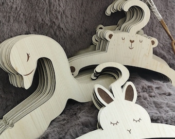 May include: A set of wooden hangers with animal designs. The hangers are made of natural wood and feature a bear, a bunny, and a swan. The hangers are perfect for organizing children's clothes.