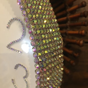 May include: Close-up of a clock face with a sparkling, iridescent crystal-covered border. The numbers 2, 3, and 4 are visible, outlined with smaller crystals. The clock's design is ornate and glamorous, with a focus on the shimmering details.