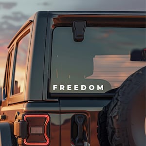 May include: A black SUV with the word "FREEDOM" in white lettering on the rear window. The image is taken at dusk, with a colorful sunset visible in the background. A spare tire is mounted on the back.