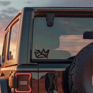 May include: Black SUV with a crown decal on the rear window. The crown is a stylized, hand-drawn design in black. The vehicle is parked outdoors with a sunset in the background.