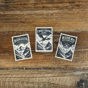 May include: Three rectangular postage stamp-style stickers featuring dark blue and cream illustrations. One depicts a mountain castle labeled Basgiath War College, another shows a dragon flying over mountains labeled Threshing Day, and the third shows crossed swords labeled Riders Quadrant.