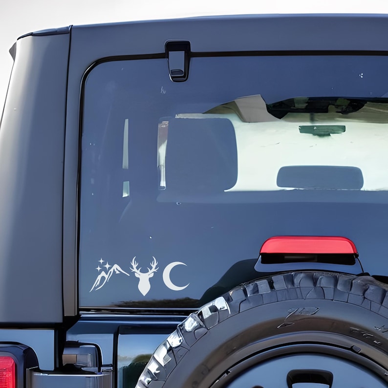 May include: A black car with a rear window sticker featuring a mountain range, a deer with antlers, and a crescent moon. The sticker is in a silver color.