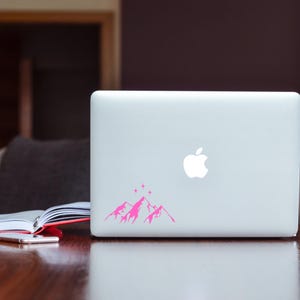 May include: A white laptop computer with a pink mountain range and stars sticker on the back.