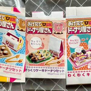 May include: Three colorful cards with Japanese text, images of donuts, and the words "Lovely Donuts". Each card features a different donut set, including a donut stand, a box of donuts, and a set of tongs. The text on the cards reads "Agetate Donut-ya-san" which translates to "Freshly Made Donut Shop".