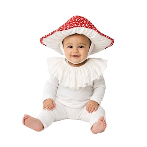 May include: A red mushroom-shaped hat with white polka dots, featuring a wide brim and a chin strap. The hat is paired with a white long-sleeved shirt and matching pants, complemented by a white ruffled collar that sits around the neck area.