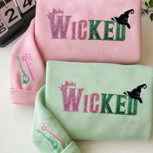 May include: Two sweatshirts, one pink and one mint green, with the word "Wicked" embroidered in glittery pink and green. A black witch hat and a crown are also embroidered on the sweatshirts. The sleeves feature a witch's broom and wand.