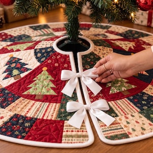 May include: A round quilted Christmas tree skirt featuring a patchwork design of red, green, and cream fabric panels with printed Christmas tree motifs. The skirt has a central opening secured by two white satin ribbon bows with white piping.