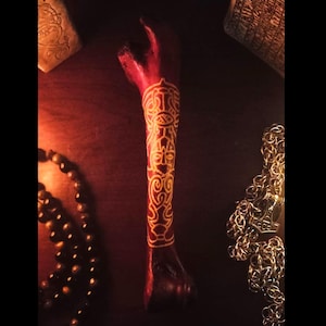 May include: A red bone with a gold design carved into it. The bone is on a dark wooden surface.