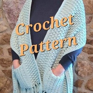 May include: A light blue crochet shawl with fringe and two pockets. The shawl is worn by a person and the text "Crochet Pattern" is superimposed on the image.