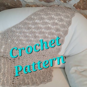 May include: A beige crochet shawl with a lacy pattern, draped over a white couch. The text "Crochet Pattern" is superimposed over the shawl in turquoise.