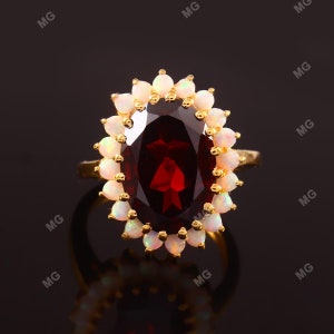 May include: A gold ring featuring a large, oval-shaped, red gemstone encircled by a halo of smaller, white gemstones.