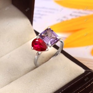 Peut inclure: Une bague en argent avec une pierre précieuse rouge en forme de poire et une pierre précieuse violette carrée.