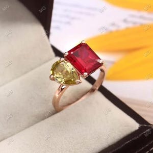 May include: A gold ring with a red emerald-cut gemstone and a pear-shaped yellow gemstone.