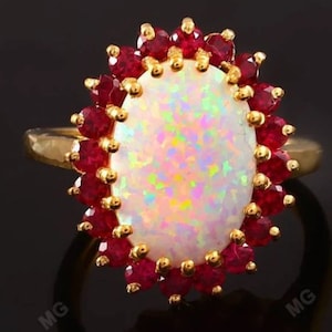 May include: A gold ring with a large oval white opal surrounded by a halo of red rubies.