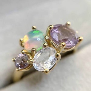May include: A gold ring with a cluster of gemstones. The ring features a large white opal, two smaller amethyst stones, and a smaller clear stone.