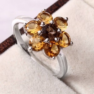 Puede incluir: Un anillo de plata con un engaste en forma de flor con seis piedras preciosas marrones y amarillas.
