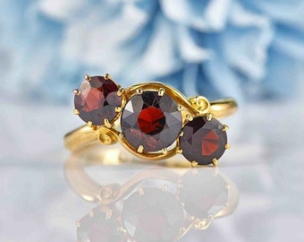 May include: A gold ring with three round red garnet stones set in a delicate, swirling design.