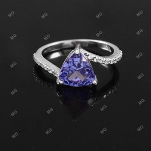 Può includere: Un anello d'argento con una pietra preziosa viola triangolare e una fila di piccole pietre preziose chiare attorno alla fascia.