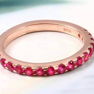Può includere: Un anello a fascia in oro rosa con una fila di piccole pietre preziose rosa brillante attorno a tutta la fascia. L'anello è contrassegnato dal numero "925" all'interno.