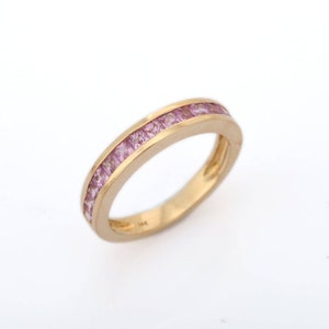 Puede incluir: Un anillo de banda de oro con una fila de piedras preciosas rosadas engastadas en un engaste de canal.