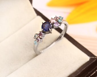 Puede incluir: Un anillo de plata con una piedra preciosa ovalada azul rodeada de piedras preciosas más pequeñas de color rosa, morado y azul.