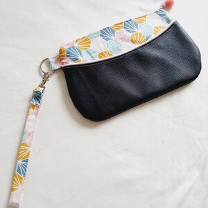 Puede incluir: Un clutch de cuero negro con un forro de tela con estampado geométrico y una correa desmontable. La tela presenta un patrón de hexágonos rosas, azules y amarillos.