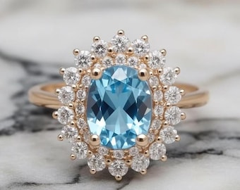 May include: A gold ring featuring a large, oval, light blue gemstone surrounded by a halo of smaller, clear gemstones. The ring's band is a simple, polished gold. The setting is intricate, with the smaller stones arranged around the central stone.
