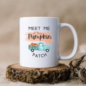 Puede incluir: Taza de café de cerámica blanca con una camioneta azul que lleva calabazas y el texto "Meet me at the Pumpkin Patch".