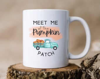 Può includere: Tazza da caffè in ceramica bianca con un camioncino blu che trasporta zucche e il testo "Meet me at the Pumpkin Patch".