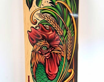 Könnte beinhalten: Ein Skateboard-Deck aus Holz mit einer farbenfrohen Illustration eines Hahns in Grün, Rot und Gelb. Der Hahn ist von goldenen und schwarzen floralen Mustern umgeben. Das Wort "Loco" ist in Rot auf der Unterseite des Decks geschrieben.