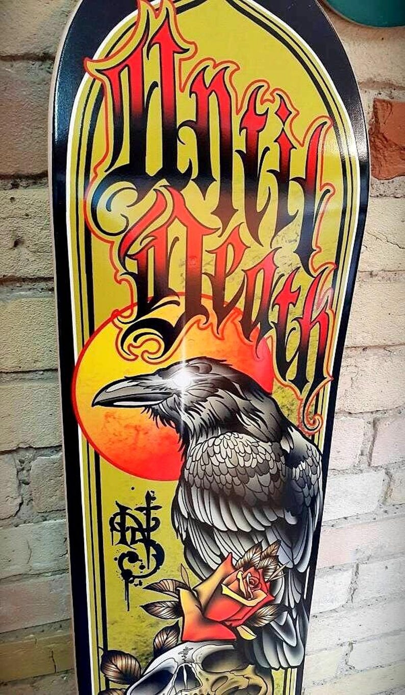 May include: A yellow and black skateboard deck with a graphic of a raven, a rose, and a skull. The text "Grim Death" is written in a stylized font.