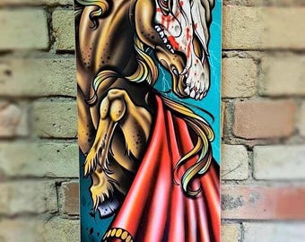 Könnte beinhalten: Ein blaues Skateboard-Deck mit einem Grafikdruck eines braunen Pferdes mit einem roten Umhang und einem Schädel. Das Pferd hat ein blutiges Gesicht und bäumt sich auf. Das Skateboard-Deck trägt den Schriftzug "Untamed" in Schwarz und Rot.