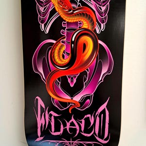 May include: Black and pink skateboard deck with a graphic of a red and yellow snake wrapped around a pink human skeleton. The text "WACO" is written in pink cursive letters.