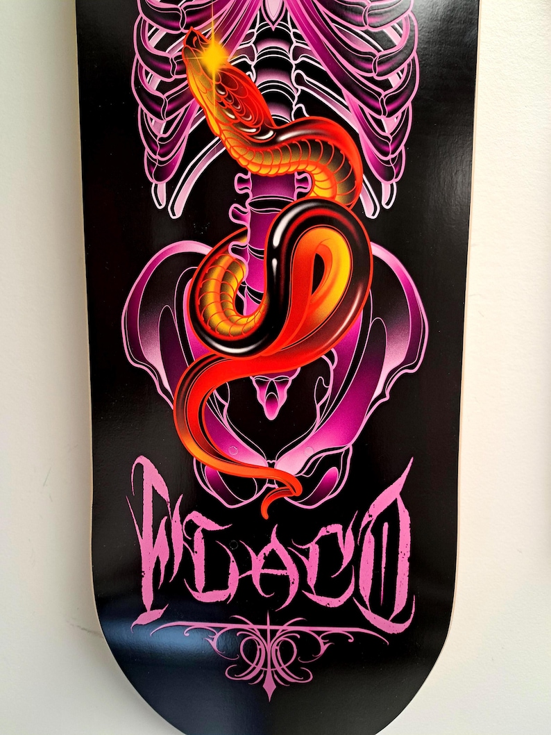 May include: Black and pink skateboard deck with a graphic of a red and yellow snake wrapped around a pink human skeleton. The text "WACO" is written in pink cursive letters.