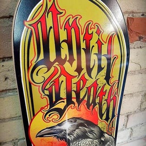 May include: A black and gold skateboard deck with a graphic of a raven and the words "Wild Death" in a stylized font.