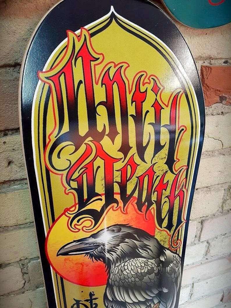 May include: A black and gold skateboard deck with a graphic of a raven and the words "Wild Death" in a stylized font.