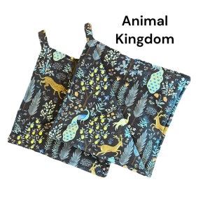 May include: Two black pot holders with a colorful animal kingdom print featuring peacocks, deer, and a leopard. The text "Animal Kingdom" is printed on the top of the pot holders.