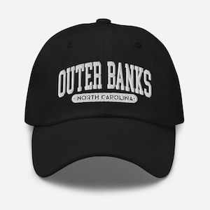 Könnte beinhalten: Schwarze Baseballkappe mit weiß gesticktem Text "Outer Banks North Carolina". Die Kappe hat einen gebogenen Schirm und eine runde Krone. Ein klassisches, lässiges Accessoire.