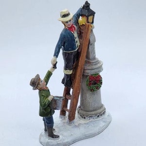 Feriendorf-Sammlung Mann, der Lampenpfahl mit Junge hilft, Weihnachtsdorf - Winterszene zu fixieren
