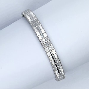 Puede incluir: Un brazalete de plata con un diseño de eslabones cuadrados.