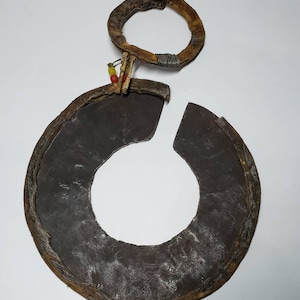 May include: A circular metal object with a leather rim and a smaller leather ring attached. The metal object is dark gray and the leather is brown with some wear. There are small red and yellow beads attached to the leather ring.