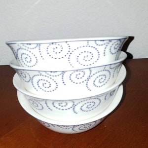 Può includere: Set di quattro ciotole in ceramica bianca con un motivo a spirale blu. Le ciotole sono impilate l'una sull'altra.