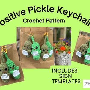 Op de afbeelding: Een haakpatroon voor een positieve augurk-sleutelhanger, met meerdere kleine, groene, getextureerde garen augurken met zwarte ogen en rood gestikte mondjes. Elke augurk houdt een klein wit bordje met tekst vast. Inclusief sjablonen en logo.
