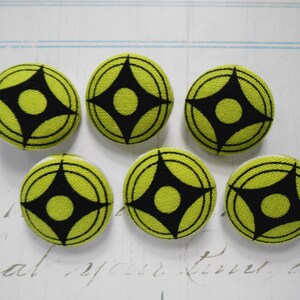 May include: Six round fabric buttons with a lime green background and a black geometric design. The buttons are arranged in a group on a white surface with faint script writing.