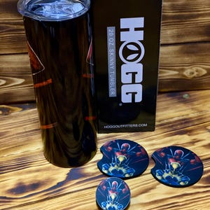 Puede incluir: Un vaso delgado negro de 591 ml con un dise&ntilde;o gr&aacute;fico colorido. El vaso est&aacute; empaquetado en una caja negra con el texto "HOGG" y "20 oz SKINNY TUMBLER" impreso en &eacute;l. La caja tambi&eacute;n incluye el sitio web "HOGGOUTFITTERS.COM". El vaso viene con tres posavasos a juego que presentan el mismo dise&ntilde;o gr&aacute;fico.