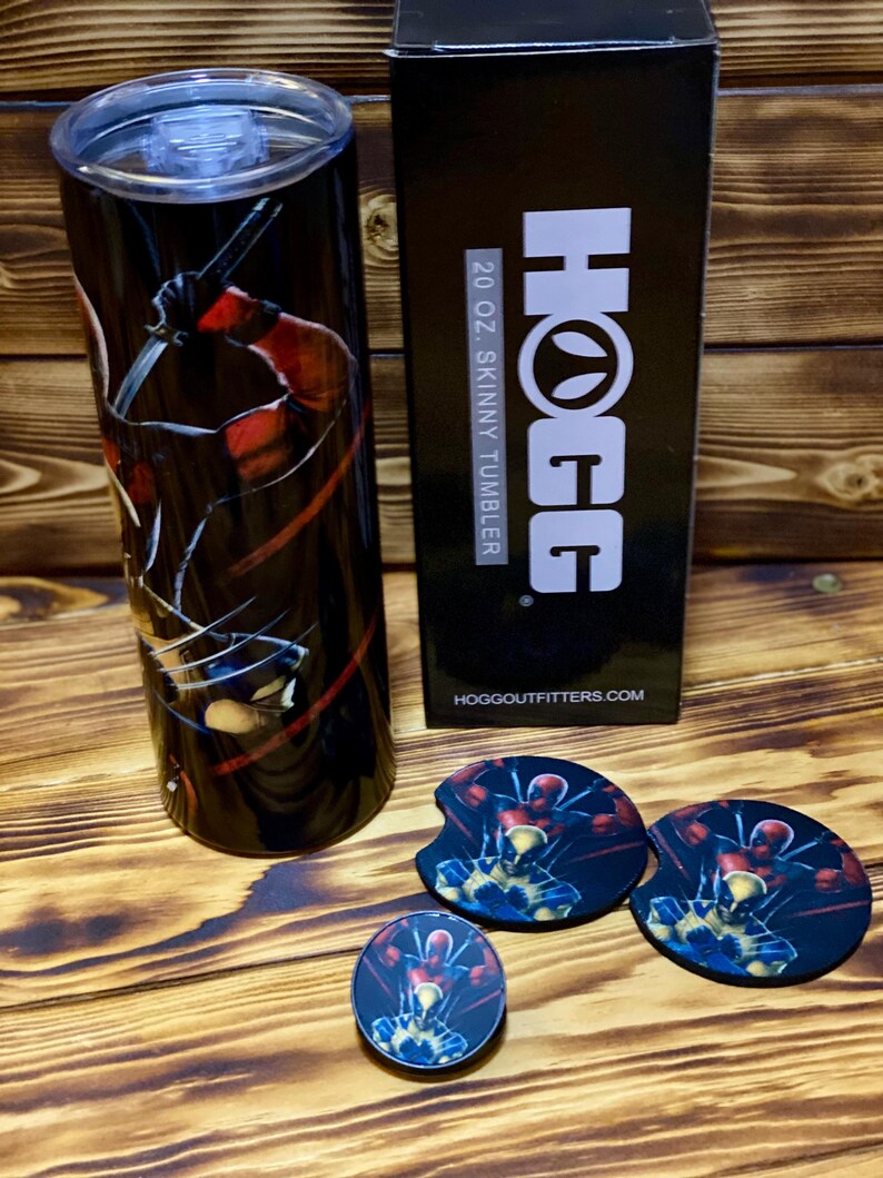 Puede incluir: Un vaso delgado de 20 onzas negro y rojo con un gr&aacute;fico de Deadpool sosteniendo una katana. El vaso est&aacute; empaquetado en una caja negra con el logotipo de HOGG y el texto "20 oz. Skinny Tumbler". La imagen tambi&eacute;n muestra tres posavasos redondos con el mismo gr&aacute;fico de Deadpool.